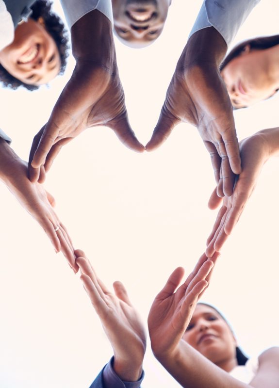 Closeup shot of a group of unrecognizable businesspeople making a heart shape with their hands outdoors